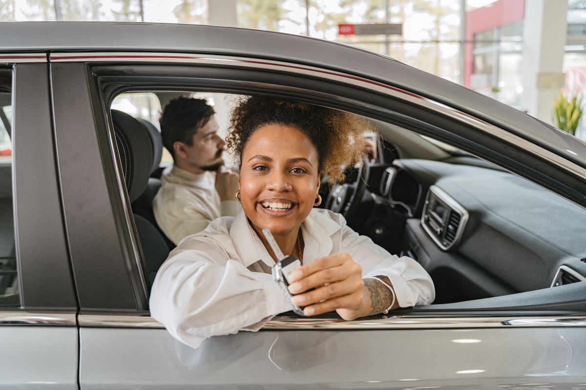 Cliente recebendo as chaves de um carro novo em uma concession&aacute;ria