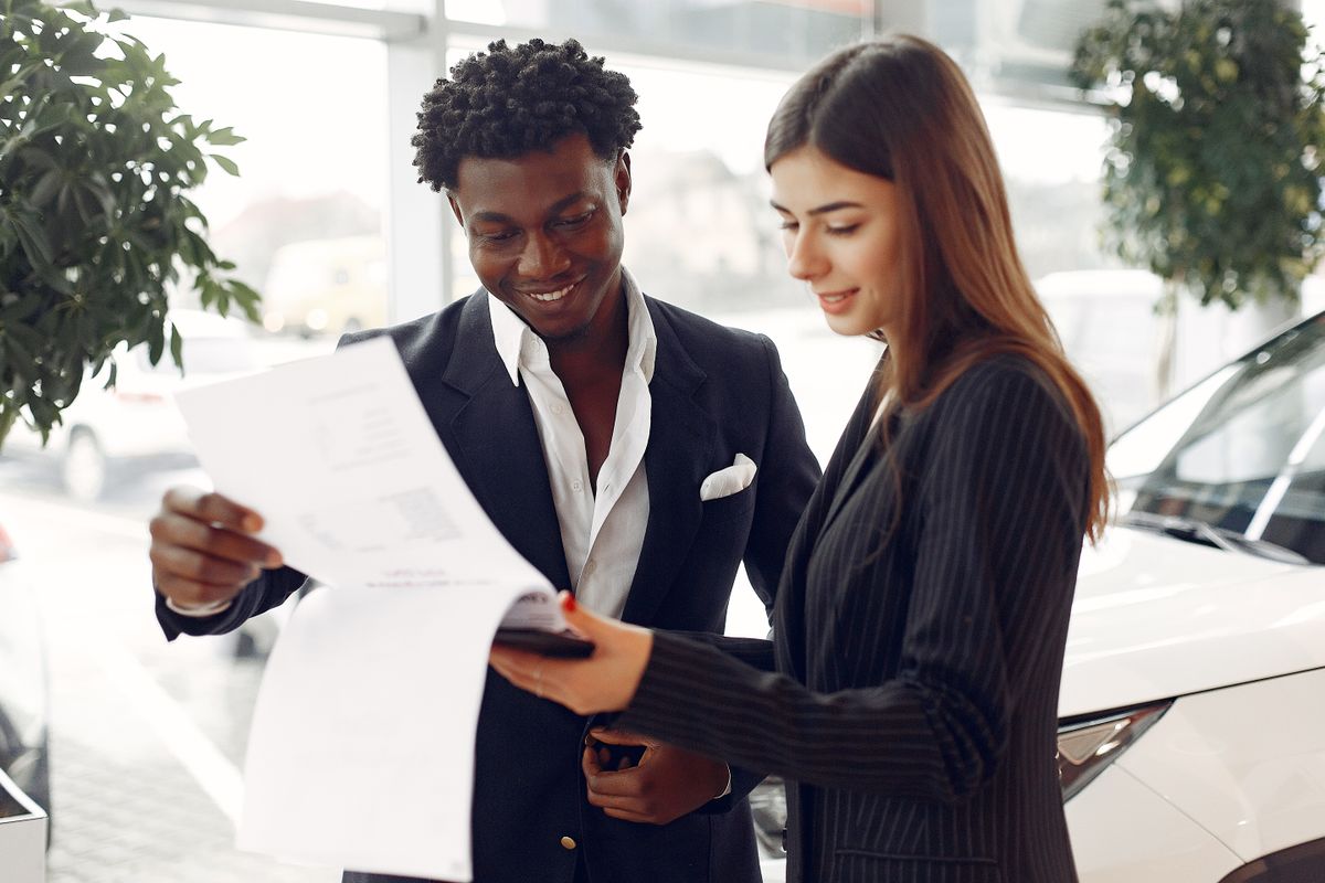 Cliente e consultor analisando documentos de um ve&iacute;culo em uma concession&aacute;ria